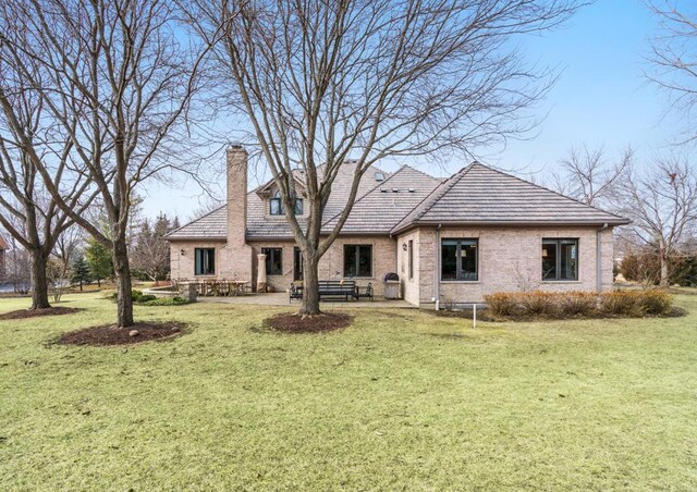 rear view of house featuring a yard, a patio, brick siding, and a chimney