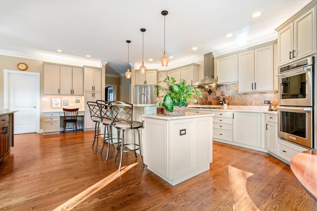 kitchen with a breakfast bar area, decorative backsplash, light wood-style floors, appliances with stainless steel finishes, and wall chimney exhaust hood