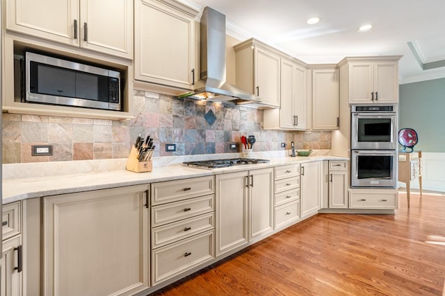 kitchen featuring light wood-style floors, appliances with stainless steel finishes, wall chimney exhaust hood, crown molding, and decorative backsplash