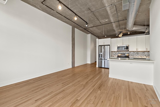 kitchen with a peninsula, stainless steel appliances, white cabinets, light wood-type flooring, and backsplash