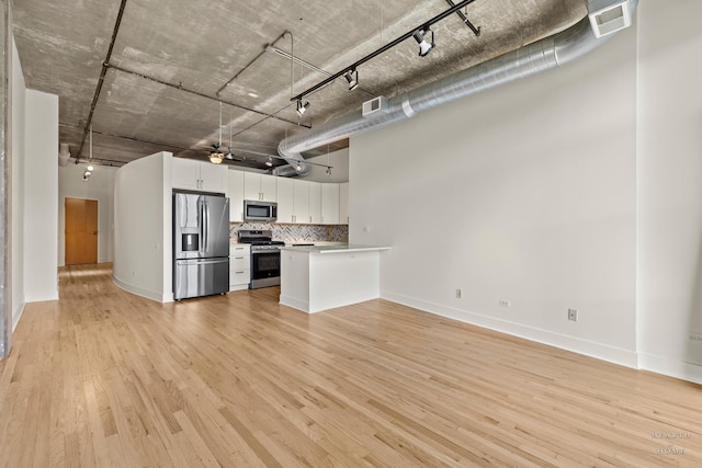 kitchen with open floor plan, white cabinetry, stainless steel appliances, light wood-style floors, and decorative backsplash