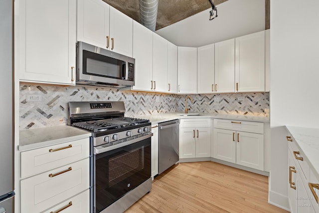 kitchen featuring light wood finished floors, a sink, white cabinets, appliances with stainless steel finishes, and tasteful backsplash