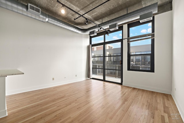 unfurnished room featuring visible vents, baseboards, floor to ceiling windows, rail lighting, and wood finished floors