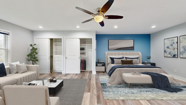 bedroom featuring a ceiling fan, wood finished floors, baseboards, recessed lighting, and two closets