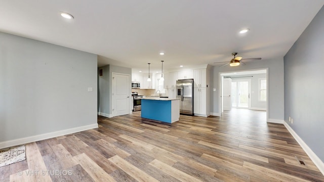 kitchen featuring wood finished floors, stainless steel appliances, white cabinets, open floor plan, and a center island