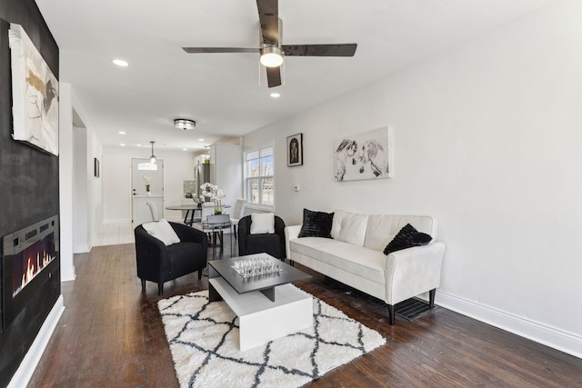 living area with baseboards, recessed lighting, a warm lit fireplace, wood finished floors, and a ceiling fan