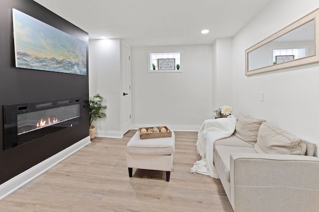 living room featuring a glass covered fireplace, recessed lighting, wood finished floors, and baseboards