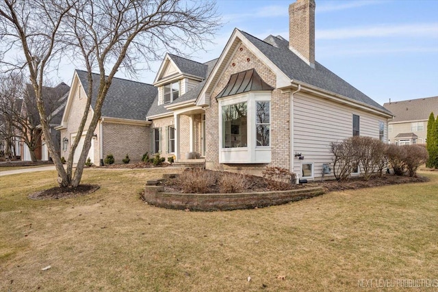 view of front facade featuring a shingled roof, a front yard, brick siding, and a chimney