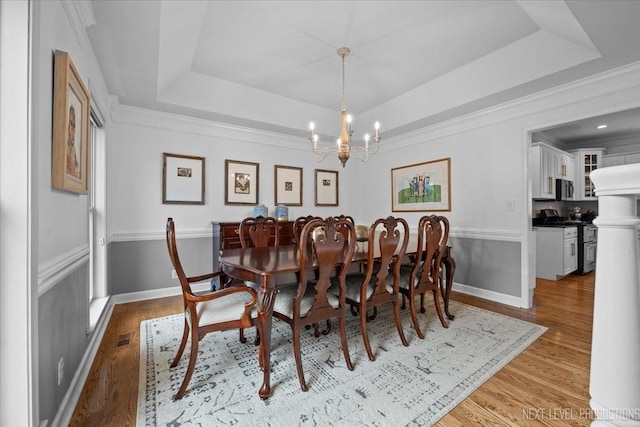 dining space with a raised ceiling, crown molding, wood finished floors, and a chandelier