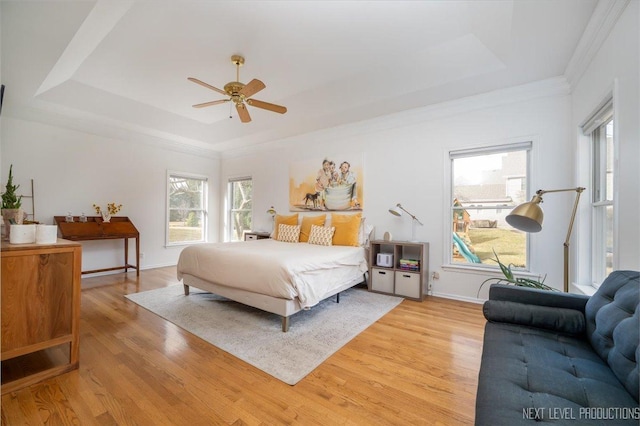 bedroom with a raised ceiling, light wood-style floors, and baseboards