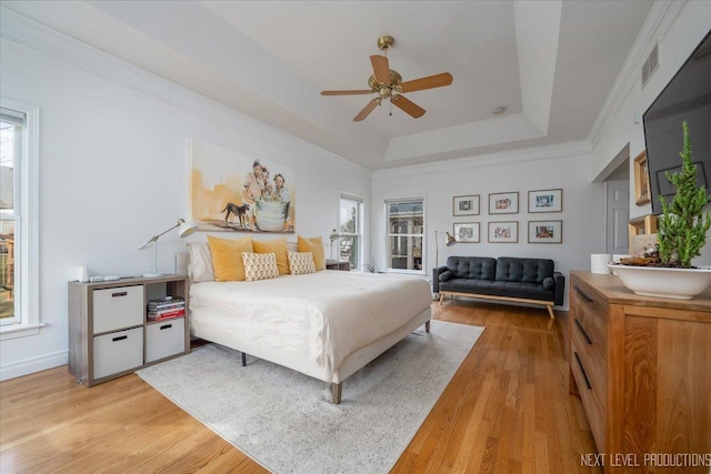 bedroom featuring visible vents, a raised ceiling, light wood-style flooring, and crown molding