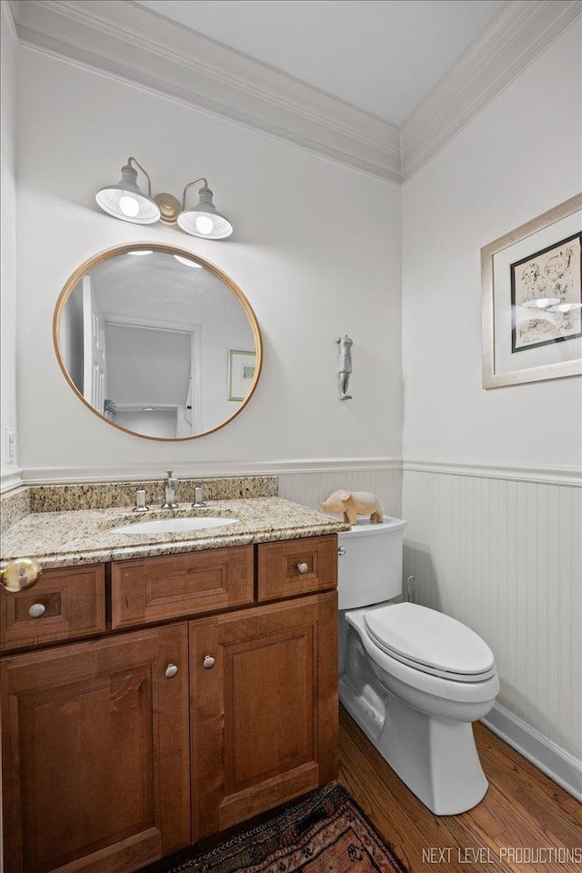 bathroom with toilet, wood finished floors, wainscoting, crown molding, and vanity