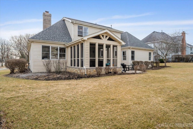 rear view of house featuring a shingled roof, a lawn, a chimney, and a sunroom