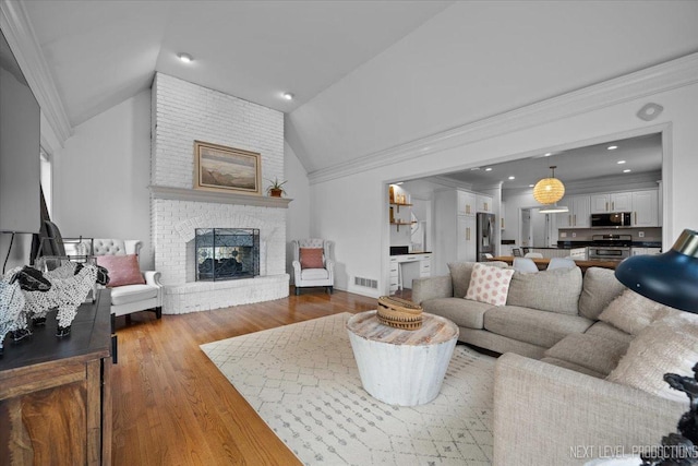 living room featuring wood finished floors, visible vents, lofted ceiling, a fireplace, and crown molding