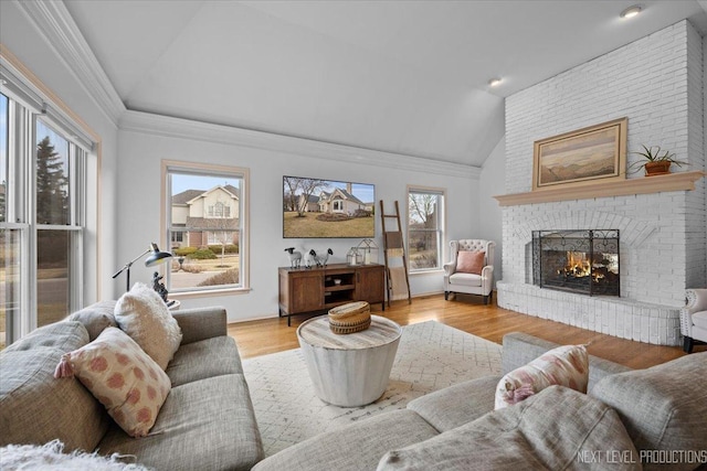 living room featuring light wood finished floors, a fireplace, crown molding, and lofted ceiling