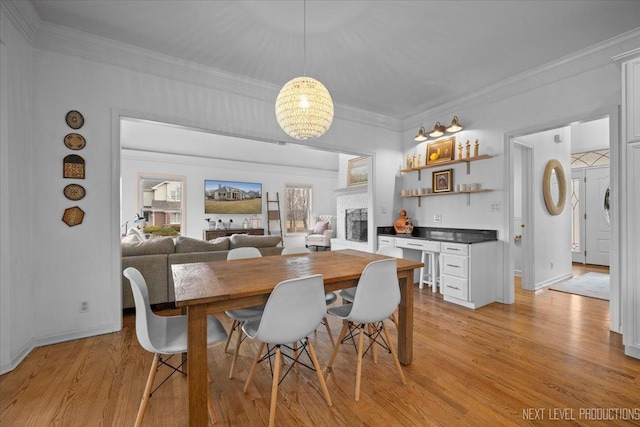 dining room with light wood-style floors, a fireplace, crown molding, baseboards, and a chandelier