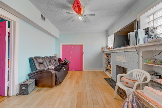 living area featuring wood finished floors, visible vents, a textured ceiling, crown molding, and a brick fireplace