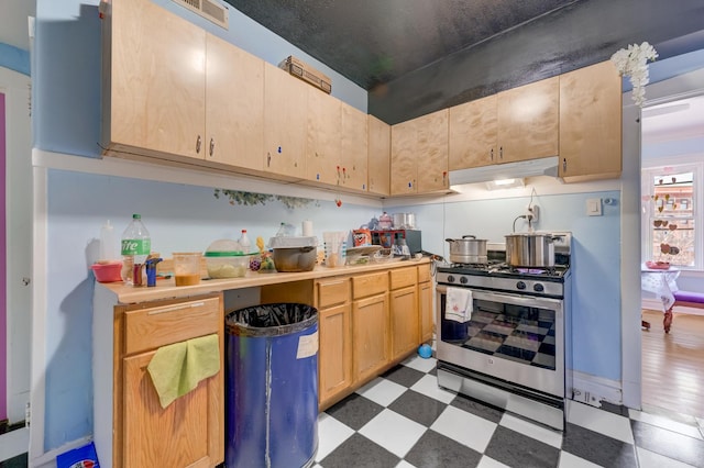 kitchen with under cabinet range hood, light floors, gas stove, and light brown cabinetry