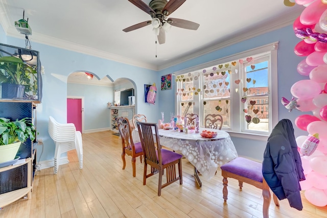 dining area with ornamental molding, a ceiling fan, hardwood / wood-style floors, arched walkways, and baseboards