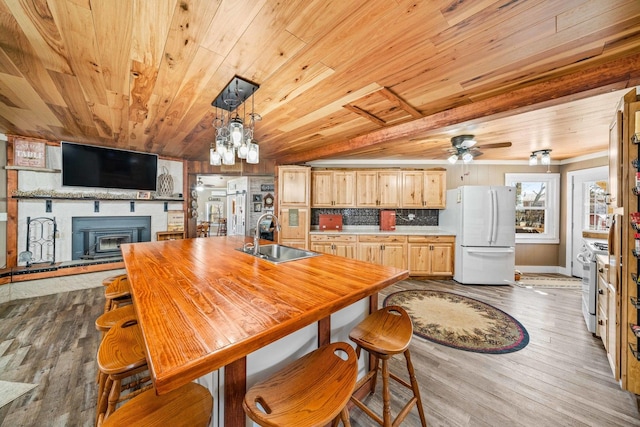 dining space featuring dark wood finished floors, wooden ceiling, a large fireplace, and ceiling fan