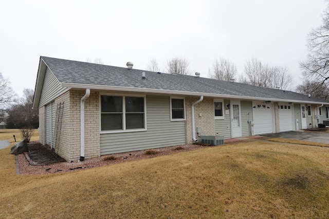 back of property featuring driveway, a yard, a garage, and roof with shingles