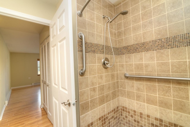 full bath with baseboards, tiled shower, baseboard heating, and wood finished floors