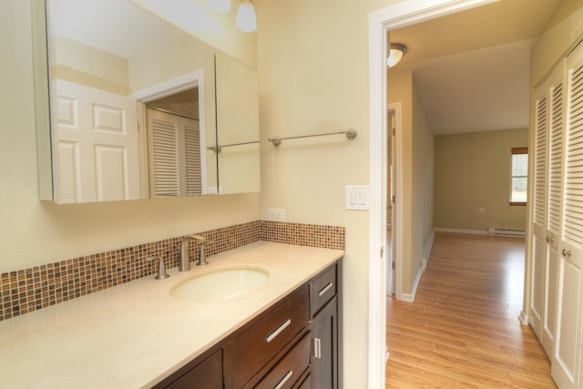 bathroom with vanity, wood finished floors, baseboards, a baseboard radiator, and decorative backsplash