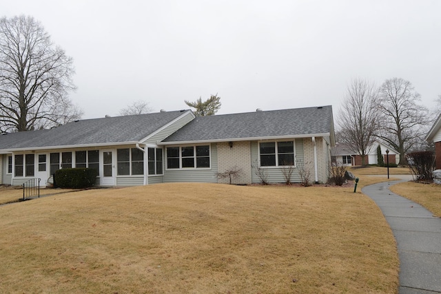 view of front of house with brick siding, a shingled roof, a front yard, and a sunroom