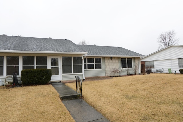 ranch-style home with brick siding, a sunroom, a front lawn, and roof with shingles