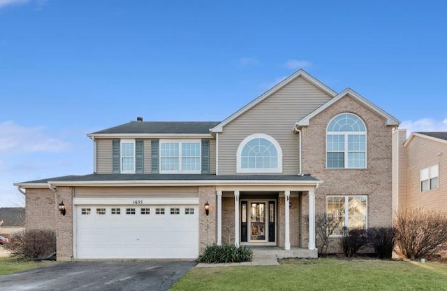 traditional-style house featuring aphalt driveway, covered porch, a front yard, an attached garage, and brick siding