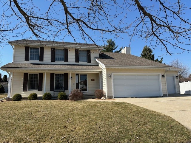 traditional home featuring a front yard, fence, driveway, an attached garage, and a chimney