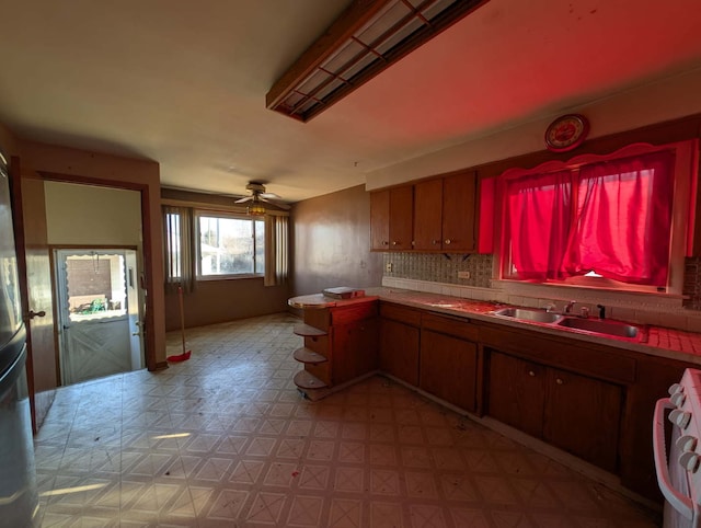 kitchen with a ceiling fan, a sink, tasteful backsplash, a peninsula, and range