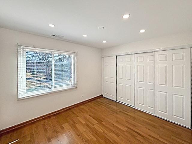 unfurnished bedroom featuring wood finished floors, visible vents, baseboards, recessed lighting, and a closet