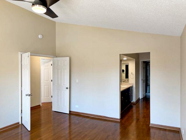 unfurnished bedroom with a textured ceiling, baseboards, dark wood-type flooring, and lofted ceiling