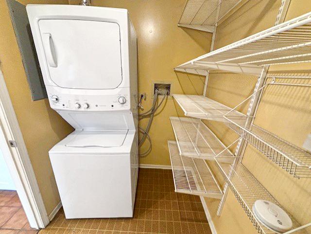 laundry room featuring tile patterned floors, baseboards, stacked washer and dryer, and laundry area