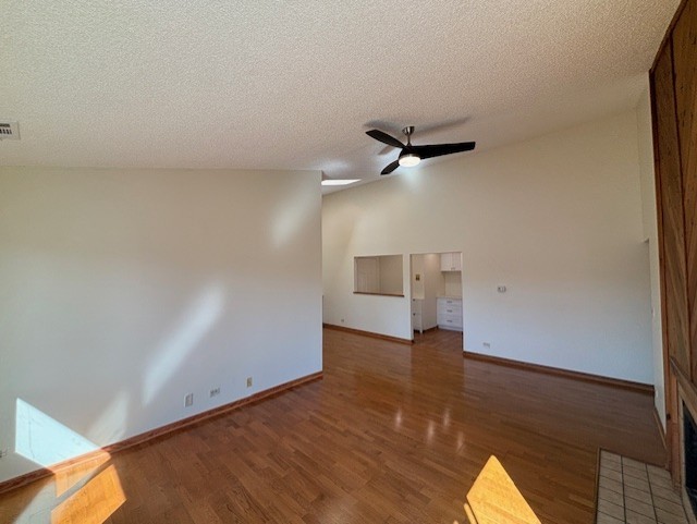 unfurnished room with visible vents, a textured ceiling, wood finished floors, baseboards, and ceiling fan