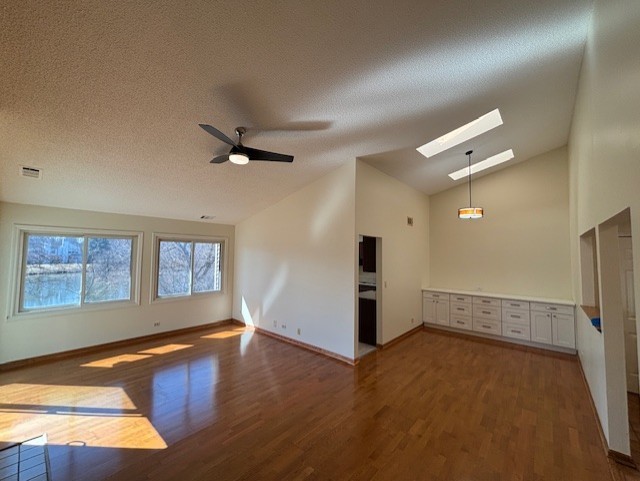 empty room featuring visible vents, a textured ceiling, wood finished floors, a skylight, and baseboards