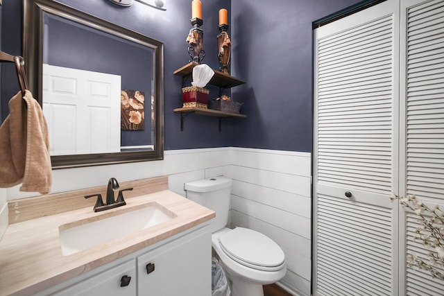 bathroom featuring toilet, wood walls, vanity, and a wainscoted wall