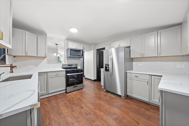 kitchen featuring light stone countertops, dark wood-style flooring, a sink, decorative backsplash, and appliances with stainless steel finishes