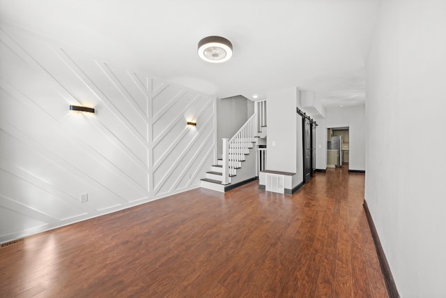 unfurnished living room with stairway, baseboards, visible vents, dark wood-style flooring, and a barn door