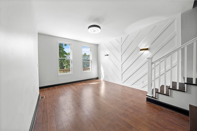 unfurnished living room with stairway, wood finished floors, visible vents, baseboards, and a decorative wall