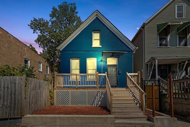 view of front facade featuring stairway, brick siding, covered porch, and fence