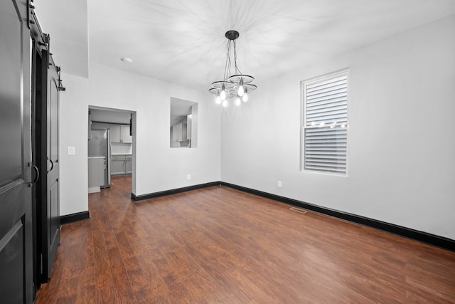 unfurnished dining area with dark wood finished floors, an inviting chandelier, baseboards, and a barn door