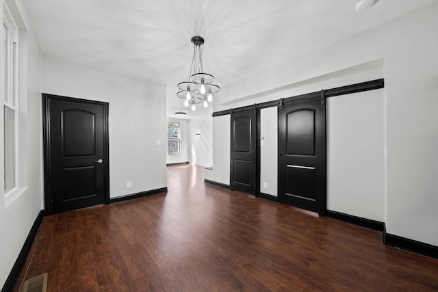 interior space with visible vents, dark wood-type flooring, baseboards, a chandelier, and a barn door