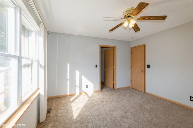 carpeted spare room featuring ceiling fan and baseboards