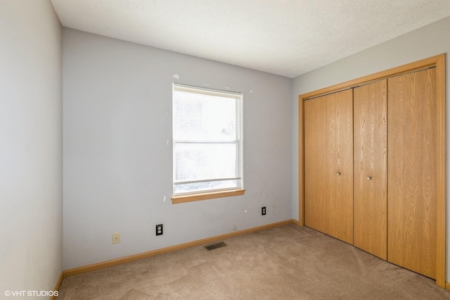 unfurnished bedroom featuring visible vents, a textured ceiling, a closet, baseboards, and light colored carpet