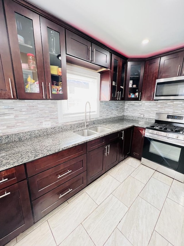 kitchen featuring backsplash, light stone countertops, stainless steel appliances, and a sink