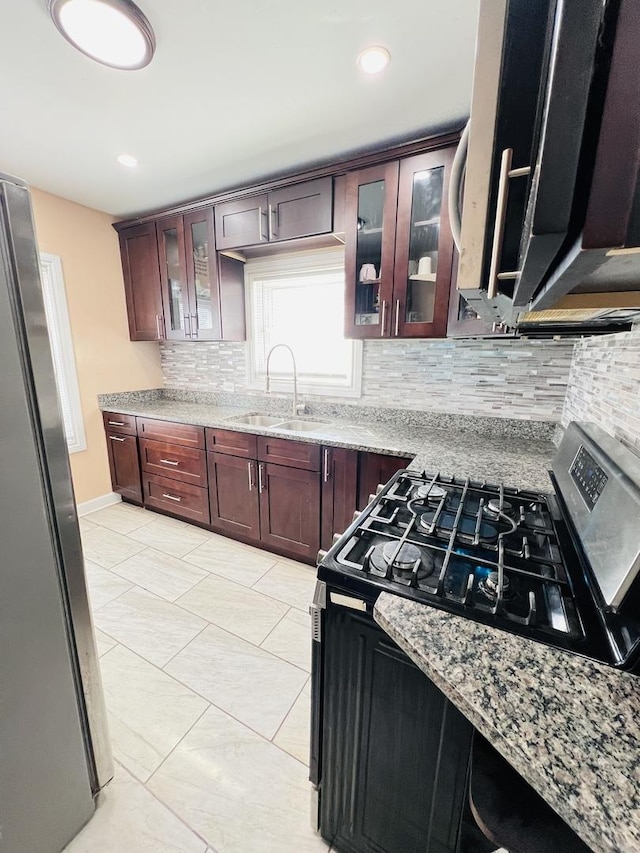 kitchen with tasteful backsplash, glass insert cabinets, light stone counters, appliances with stainless steel finishes, and a sink