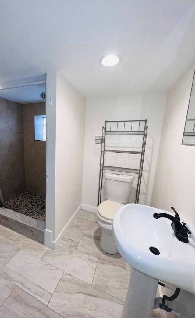 bathroom featuring toilet, tiled shower, marble finish floor, and baseboards