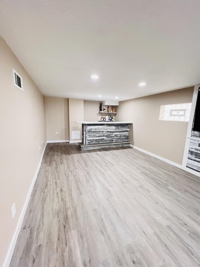 finished below grade area with visible vents, baseboards, a bar, and wood finished floors